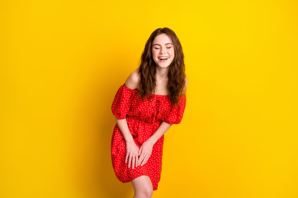 穿着红色花纹裙子的时尚女孩在明亮的黄色背景前欢笑的照片肖像图片下载