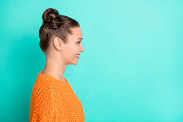 侧面肖像照片，女孩穿着毛衣，留着女孩气质的发型，微笑着望向空旷的空间，背景为鲜艳的青色。图片下载