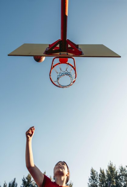 女孩在户外篮球场上朝着篮筐投掷篮球，清澈的蓝天下，动态向上的角度，篮球接近篮筐，青少年运动，激励，运动品牌，运动模糊。图片下载