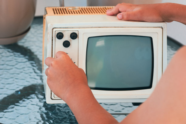 一个人的手正在调整一台放在玻璃桌上的老式复古电视，唤起了一种怀旧感和与过去科技的联系。图片下载