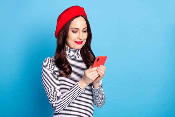 身穿贝雷帽的女性在鲜艳的蓝色背景下微笑着使用手机的肖像照片图片下载