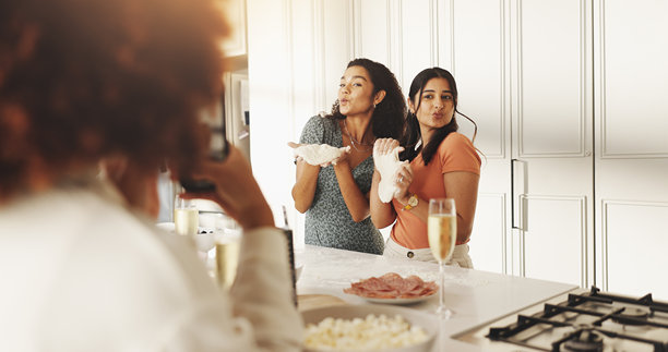 女性、朋友们在家中快乐地用照片、手机和面团烹饪，撅嘴并在网上发布。人们、团体和食谱在厨房中亲吻、撒面粉和准备食材，分享美食于社交网络。图片下载