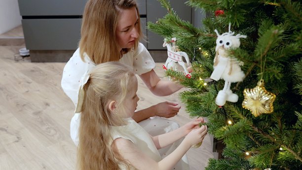 母女俩在柔和灯光的客厅里装饰松树圣诞树，使用复古木制玩具和金色装饰品，分享温馨的节日时刻。图片下载