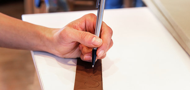 一位艺术家正在用笔和尺子在一块油毡上绘制圆形图案的特写。学生的手正在手绘印刷设计。图片下载