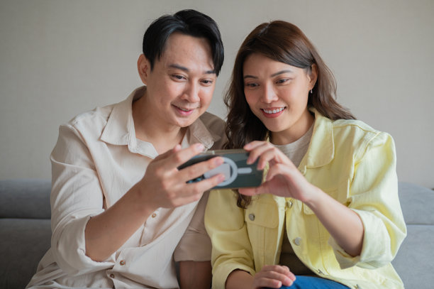 亚洲华人情侣在家沙发上享受周末时光，一起使用智能手机的照片图片下载