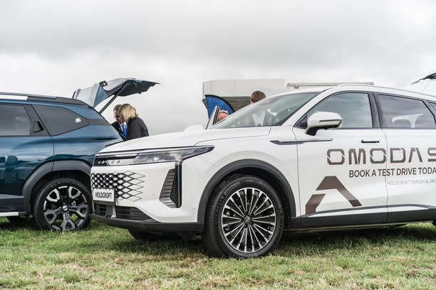 一辆白色的Omoda 9在南特威奇展会上展出，背景中有人在浏览汽车。图片下载