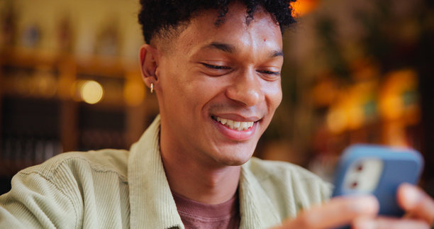 男人在咖啡馆里微笑着用智能手机发短信，正在与联系人交流，打字并在餐厅上网。这个人正在咖啡店里用手机查看社交媒体，笑着看搞笑图片，搜索和检查帖子。图片下载