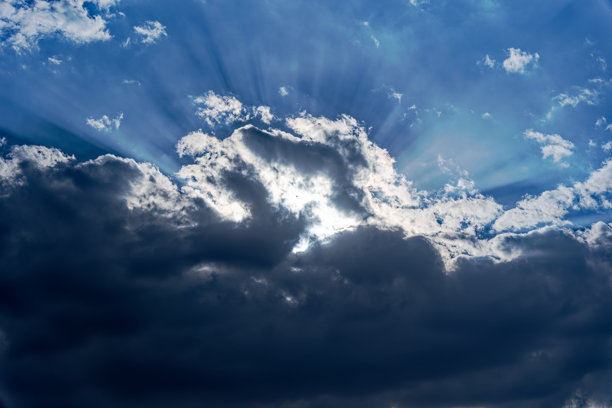这张照片展示了一个戏剧性的天空，云层中有深色和浅色的云朵。明亮的阳光透过云层，形成了惊艳的光辉和神圣的光效。图片下载