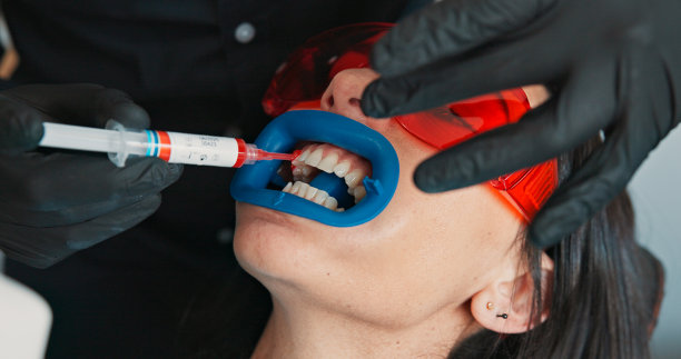 牙科诊所内，戴着护目镜的医生与女性患者进行检查或牙齿美白。牙科卫生员、医疗专业人员与女性在诊所进行口腔检查。图片下载