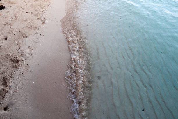 这张图片展示了一个宁静的海滩场景，温柔的海浪拍打着沙滩。图片下载