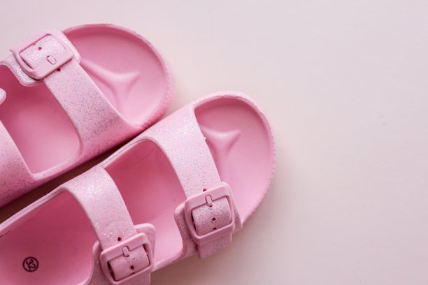 一双粉色闪亮的儿童凉鞋，带有扣子，斜放在柔和的粉彩表面上。适合儿童服装、夏季或时尚设计主题的俯视照片。图片下载