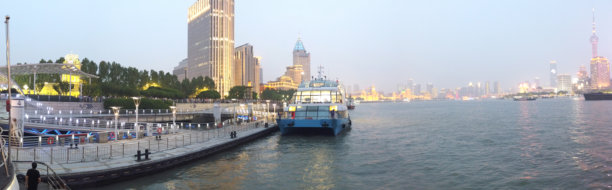 黄昏时分城市海滨的全景照片，码头上停着一艘蓝色船只，摩天大楼灯光璀璨。图片下载