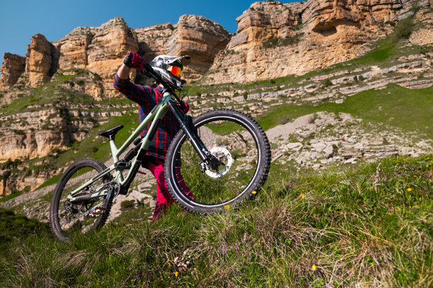 骑自行车的运动员戴着头盔，站在山地车上休息，准备下坡，背景是壮丽的山脉和风景。山地自行车下坡项目的背景。图片下载