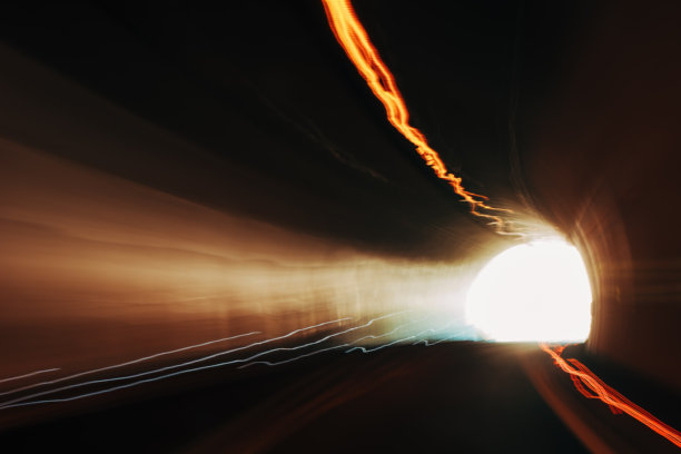 长时间曝光的隧道照片，伴随光轨和明亮的出口光芒，营造出动态的运动模糊和戏剧性的视觉效果。图片下载