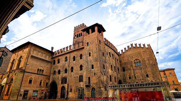 博洛尼亚市中心的阿库尔索宫和恩佐国王宫的广角照片，展示了中世纪砖砌建筑、城垛和市政建筑，背景是阴云密布的天空，体现了文化遗产和欧洲城市旅游的概念。图片下载