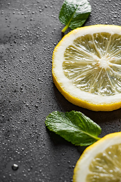 新鲜多汁的柠檬片在黑色背景上。鸡尾酒配料 - 薄荷叶和柠檬。成熟柠檬上的水滴。食品背景。竖版照片。图片下载