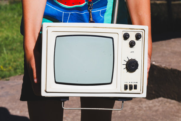 一个年轻人手持一台黑白屏幕的便携式复古电视。这张图片展示了过去技术与现代的结合，唤起了对童年的怀旧情感。图片下载