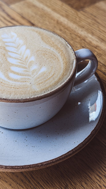 桌子上半个陶瓷咖啡杯的竖直照片，杯中盛有卡布奇诺。图片下载