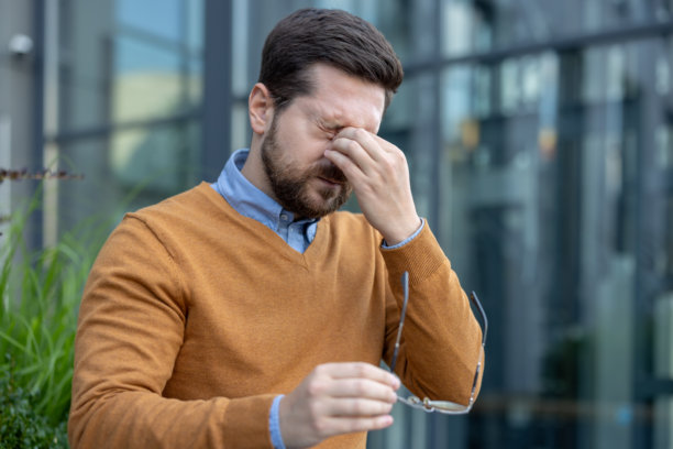 年轻男性商人在工作大楼外的街道上坐着，手中拿着一副眼镜，因疲劳而揉眼睛的特写照片图片下载