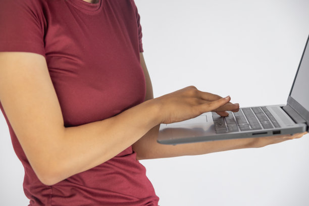 一张聚焦的照片捕捉到一个穿着深红色上衣的人，熟练地操作着一台银色的笔记本电脑。图片下载