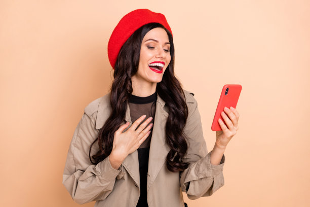 在淡米色背景下，手持手机的女孩笑容灿烂的肖像照片图片下载