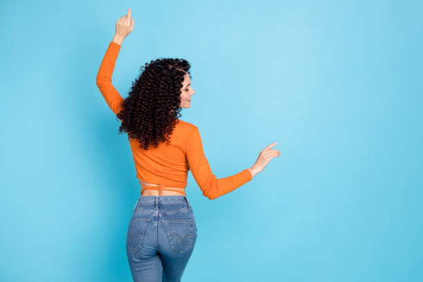 穿着短款上衣的卷发女性在明亮的蓝色背景下跳舞的罕见视角照片图片下载