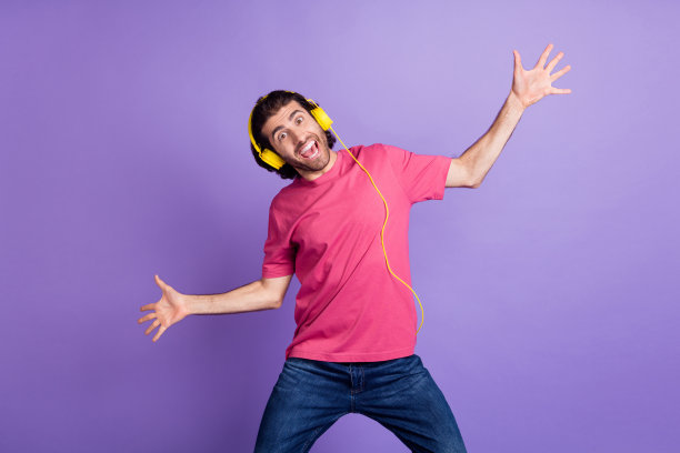 乐观的棕发男孩穿着粉色T恤，戴着耳机在淡紫色背景下跳舞的照片图片下载