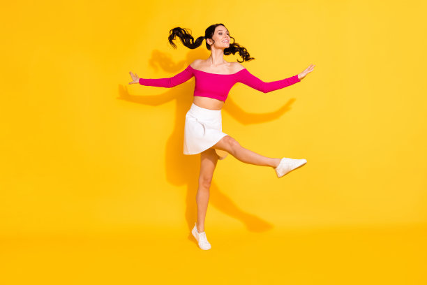 年轻快乐女孩的全身侧面照片，面带微笑，享受乐趣，背景为黄色。图片下载