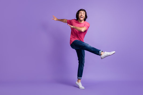 穿着粉色服装的可爱时尚年轻男孩在紫色背景下跳舞走动的全身照片图片下载