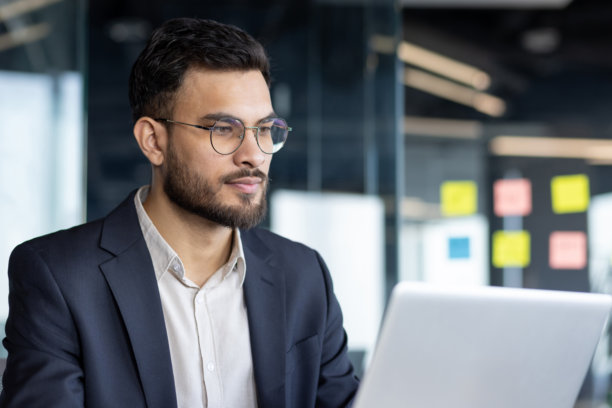 专注自信的商人在工作中的特写照片，思考的男人正在阅读电子报告。商人在办公室内使用电脑工作。图片下载