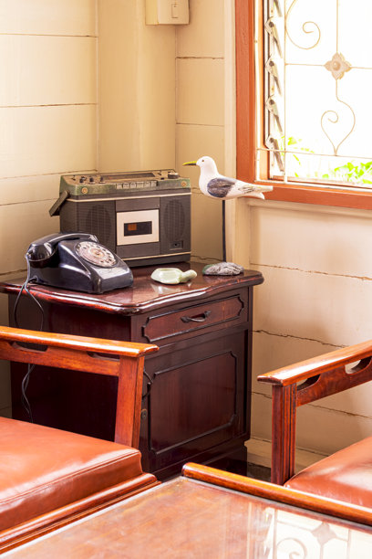 老式收音机、拨号电话和装饰娃娃放在柚木柜子上，客厅内有一套桌子，整个房间呈现复古风格，墙上挂着竖框画。图片下载