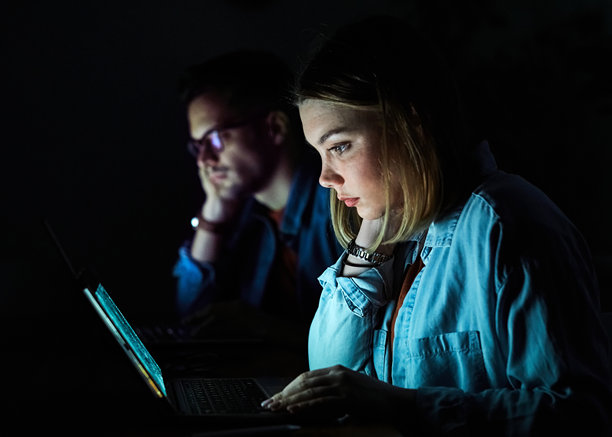 年轻的商业朋友在夜晚的办公室里，情侣学生使用笔记本电脑，商人和商女人在看电视，享受电影，创业的晚上，屏幕发出柔和的光。图片下载