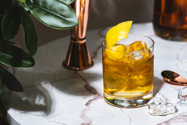 复古风格的鸡尾酒，配有龙舌兰酒、苏打水、冰块和柠檬。大理石桌子上摆放着绿色植物。图片下载