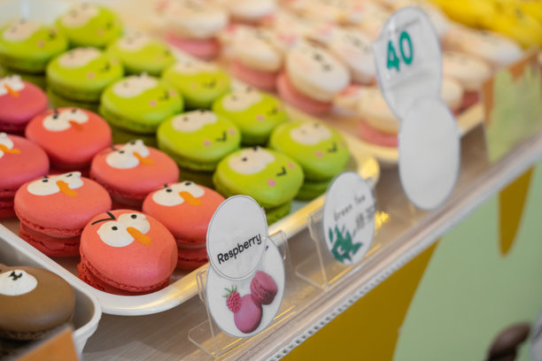 这张图片展示了装满色彩缤纷的角色主题马卡龙的托盘，这是一种法国甜点，基于蛋白霜制作。马卡龙被装饰成可爱的卡通面孔。图片下载