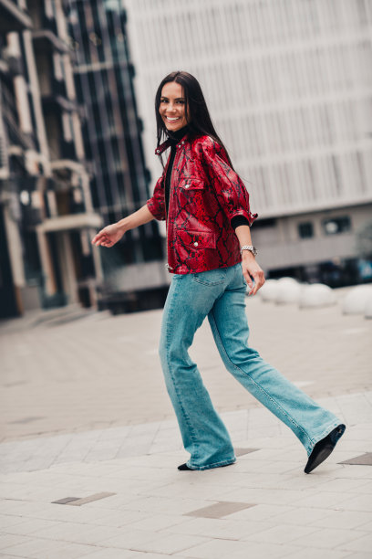 时尚女性在城市中行走，穿着时髦的红色夹克和牛仔裤，展现都市时尚与自信优雅，竖版照片图片下载