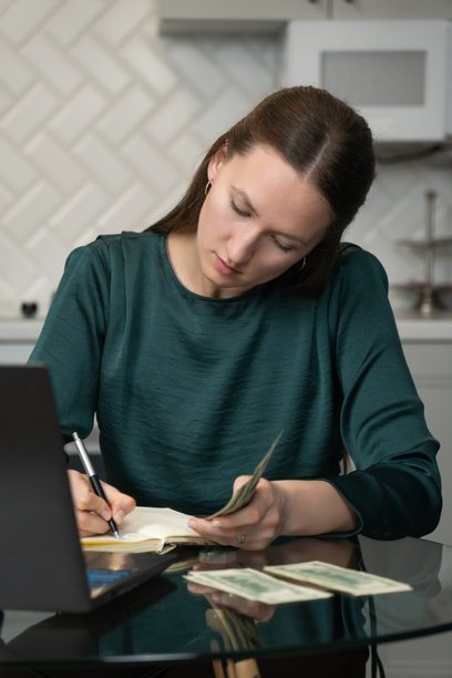 专注的年轻女性自由职业者在家远程工作，计算收入和支出，管理财务，清点现金并在笔记本上做记录。竖版照片图片下载