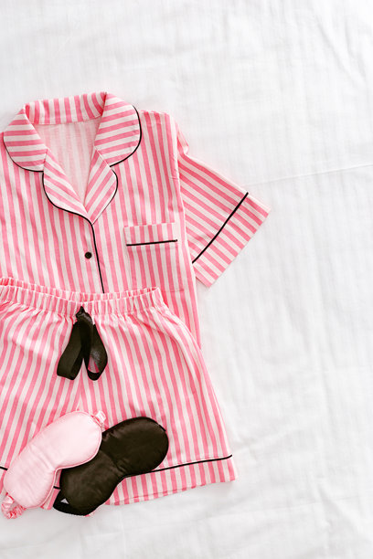 俯视折叠的鲜艳粉色女性睡衣，搭配黑色和粉色的缎面睡眠眼罩，放在白色床上。明亮的平铺舒适睡衣，适合睡眠和放松。时尚睡衣的美学生活方式照片。图片下载