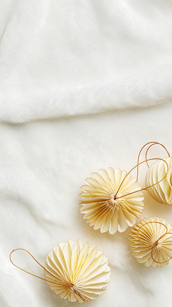 平铺的纸质新年装饰品，金色米色圣诞球放在白色毛皮背景上，冬季节日静物。简约照片，优雅的节日装饰，俯视图，留白，手机格式。图片下载