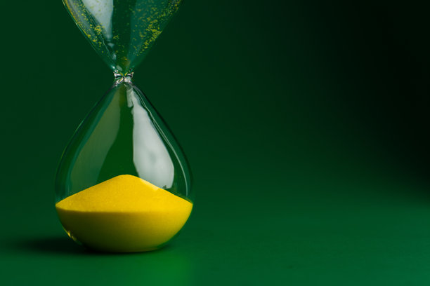 绿色背景上的黄色沙漏特写照片。质量工作和时间管理的概念。图片下载