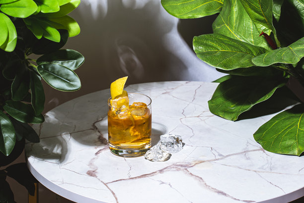 复古风格的鸡尾酒，配有龙舌兰酒、苏打水、冰块和柠檬。大理石桌子上摆放着绿色植物。图片下载