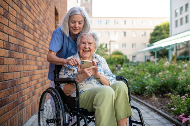 坐在轮椅上的老年患者向护理人员展示智能手机中的图片。图片下载