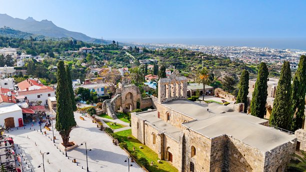 贝拉帕伊斯修道院和传统塞浦路斯村庄的鸟瞰图，周围环绕着郁郁葱葱的绿树和山坡，位于北塞浦路斯基尔尼亚，适合旅行和纪录片使用的历史建筑和文化遗产照片。图片下载