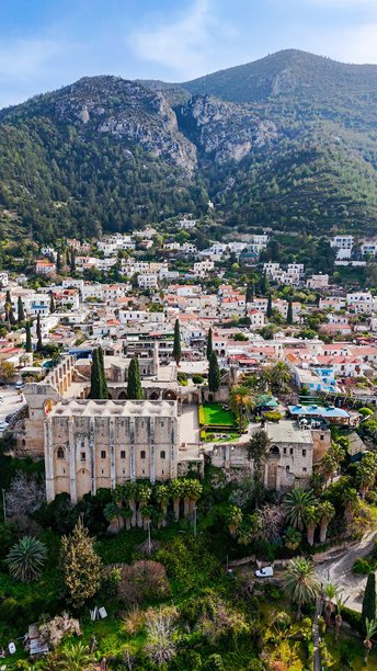 贝拉帕伊斯修道院和传统塞浦路斯村庄的鸟瞰图，周围环绕着郁郁葱葱的绿树和山坡，适合旅行和纪录片使用的历史建筑和文化遗产照片。图片下载