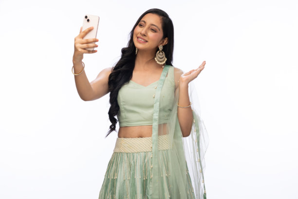 穿着传统服装的美丽女性在白色背景下庆祝排灯节，使用手机拍照的照片图片下载