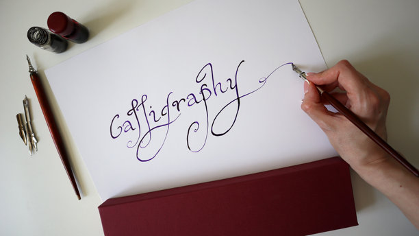 书法过程的照片。女性的手在书写“书法”这个词。手写字体。墨水，钢笔。白色背景。图片下载