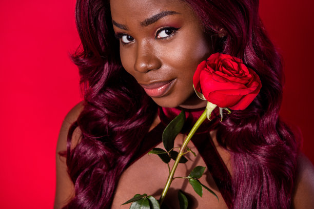 剪裁的照片，非裔美国人迷人的漂亮女性面孔，手持玫瑰，梦幻般的红色背景。图片下载