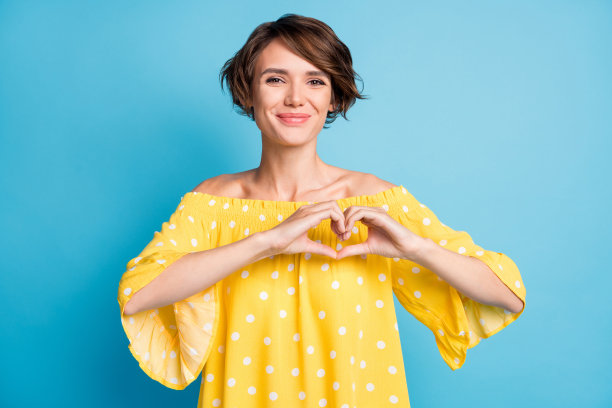 可爱的女孩在鲜艳的蓝色背景下用双手做出心形手势的照片肖像图片下载