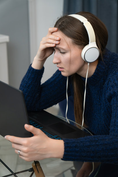 年轻女性戴着耳机，头痛地在家远程工作，手触摸额头，承受着压力和紧张。竖版照片图片下载