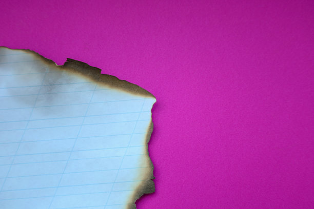 一张烧焦的有线纸边缘放在明亮的粉红色背景上，形成了一幅戏剧性和概念性的图像。照片强调了完美背景与受损烧焦纸之间的对比。图片下载