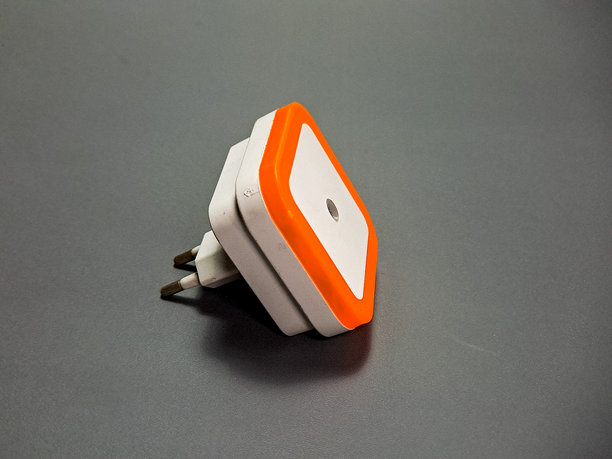 这张图片展示了一个现代、棱角分明的白色和橙色夜灯，放置在灰色表面上，其流线型设计兼具实用性和氛围照明。图片下载